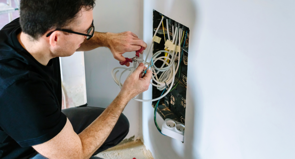 A man is working on a complex network of cables inside a wall.